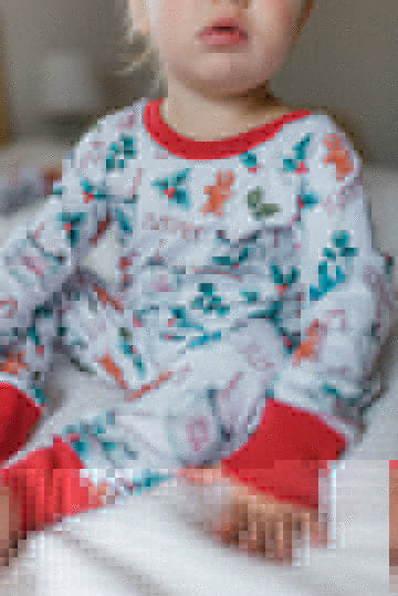 baby girl wearing personalized Christmas PJ's with images of hot cocoa, gingerbread men, and holly leaves on a white background and red cuffs.