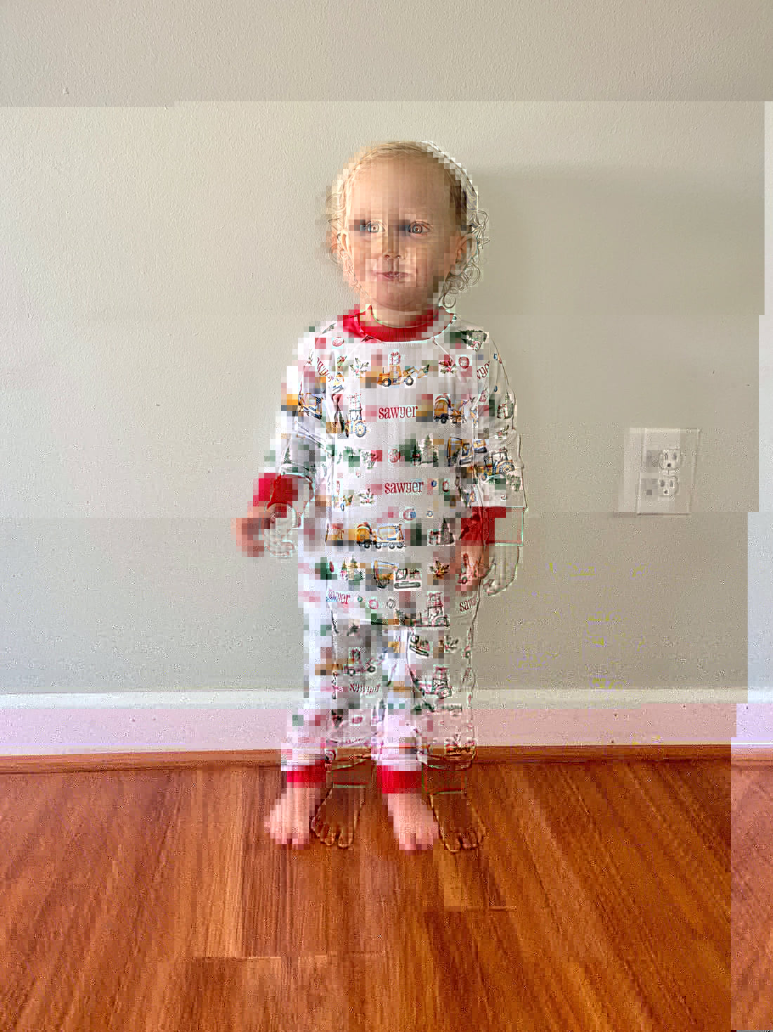 little boy wearing Christmas Construction custom holiday pajamas with construction vehicles in santa hats and christmas trees, featuring child's name in red letters and red cuffs.