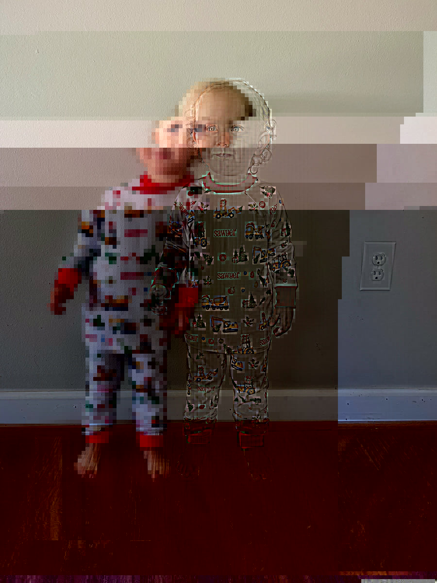 little boy wearing Christmas Construction custom holiday pajamas with construction vehicles in santa hats and christmas trees, featuring child's name in red letters and red cuffs.