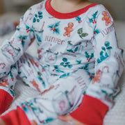 baby girl wearing personalized Christmas PJ's with images of hot cocoa, gingerbread men, and holly leaves on a white background and red cuffs.