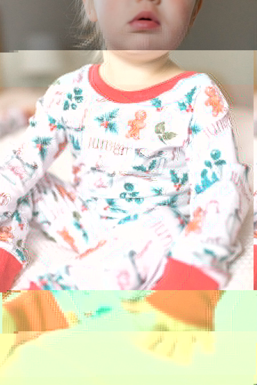 baby girl wearing personalized Christmas PJ's with images of hot cocoa, gingerbread men, and holly leaves on a white background and red cuffs.